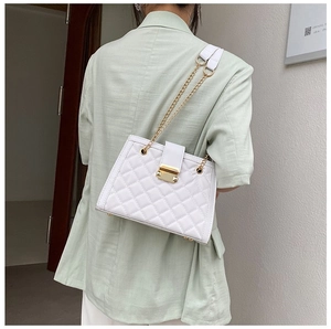Close-up of white quilted crossbody bag featuring gold chain strap and metal lock detail