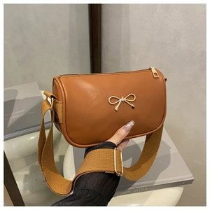 Detail of brown PU leather bag featuring a gold bow accent and wide woven canvas strap
