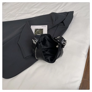 Close-up of black leather bag with silver grommet details and metal chain on grey blazer