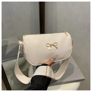 Detail of a beige handbag featuring a gold bow buckle and a wide woven shoulder strap