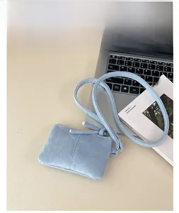 Blue suede mini crossbody bag with zipper detail placed on a laptop and magazine