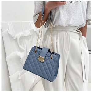Detail of blue quilted chain shoulder bag featuring gold clasp and accordion side structure
