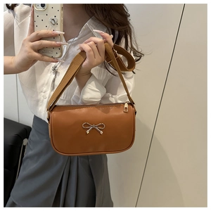 Detail view of brown PU leather shoulder bag featuring a slim golden bow buckle and strap