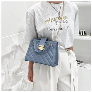 Detail of blue quilted shoulder bag featuring gold chain strap and metal lock closure