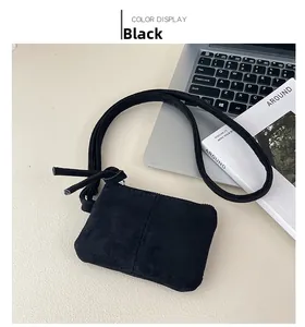 Detail of a minimalist black suede mini crossbody bag on a desk with a laptop