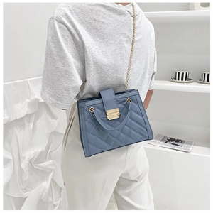 Detail of blue quilted shoulder bag featuring gold chain strap and metallic lock closure