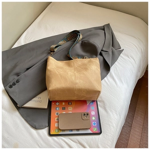 Macro detail of tan leather tote bag with ethnic woven wide strap next to a tablet