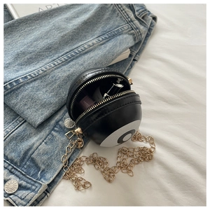 Detail of spherical black and white crossbody bag with gold chain strap on blue denim