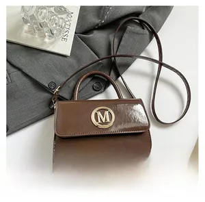 Gros plan du mini sac en cuir verni marron avec logo M doré et bandoulière fine