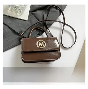 Sac à main en cuir verni marron avec boucle M dorée et bandoulière à côté d'un téléphone