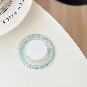 Detailed view of white circular phone grip with light green pearls on a white desk