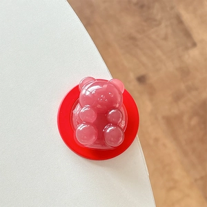 Close-up of a 3D pink resin bear phone grip with a red base on a white desk