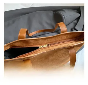 Detail of a large brown tote bag showing smooth leather straps and secure metal zipper closure