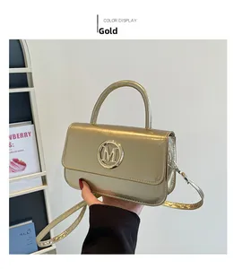 Détail macro du sac en cuir métallisé doré avec logo M et poignée supérieure polie