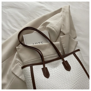 Dettaglio borsa shopper bianca intrecciata con manici in pelle marrone su blazer beige