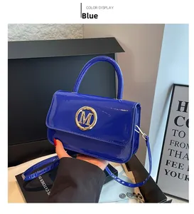 Détail d'un sac à main bleu brillant en cuir verni avec boucle M dorée et bandoulière