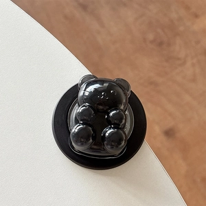 Detail shot of a glossy black bear magnetic phone stand on a white desktop background