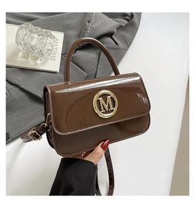 Détail de la texture en cuir verni marron brillant et logo M doré sur un sac de luxe