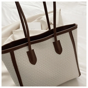 Dettaglio della borsa tote intrecciata crema con manici in pelle marrone e texture