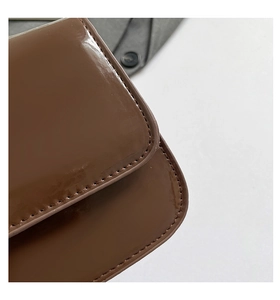 Détail de la matière en cuir verni marron foncé brillant avec coutures sur un sac rétro