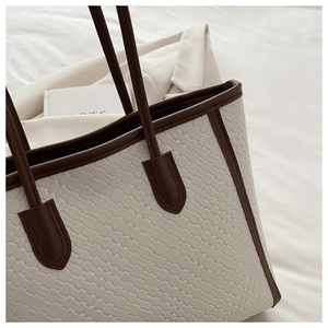 Dettaglio borsa tote beige intrecciata con manici in pelle marrone scuro e finitura