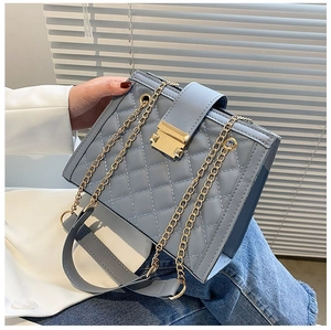 Detail view of quilted blue grey shoulder bag featuring gold chain and square buckle