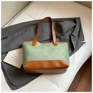 Close-up of green canvas tote bag with brown leather contrast base and handles for work