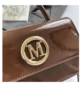 Détail du sac à main en cuir verni marron avec boucle dorée circulaire lettre M