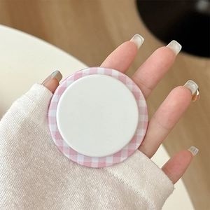 Detailed close-up of a pink gingham MagSafe phone grip being held by hand on a desk