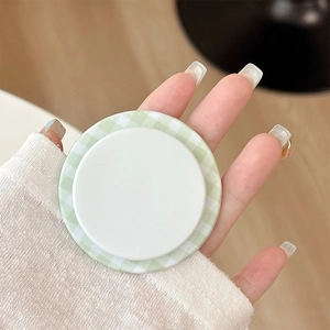 Close-up of a hand holding a green checkered magnetic phone grip for stable mobile support