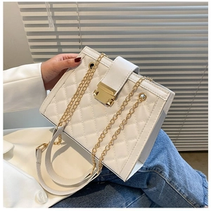 Detail of white quilted handbag with golden twist lock and chain strap held by model