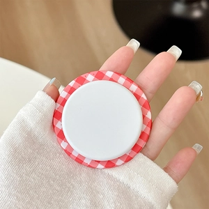 Close-up of red and white checkered magnetic pop-up phone grip held between fingers