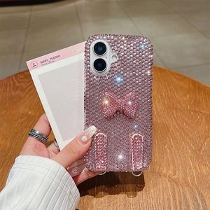 Pink rhinestone phone case with bow and lanyard rings shown in hand on wooden table