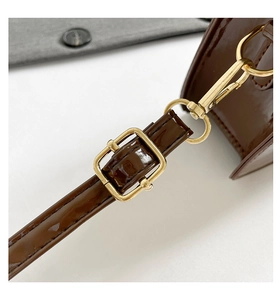 Détail d'une bandoulière en cuir verni marron foncé avec boucle et fermoir dorés