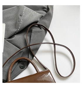Détail d'un sac à main en cuir verni marron foncé avec coutures et finition brillante