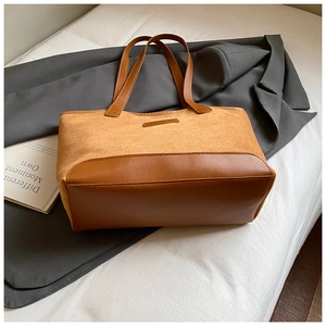 Detail of caramel brown tote bag featuring suede and leather patchwork on white bedding