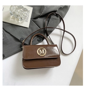 Détail d'un petit sac à main en cuir verni marron avec logo M doré et style urbain chic