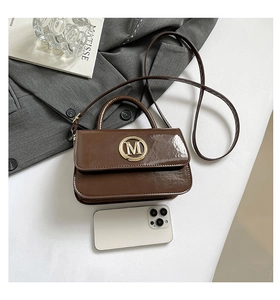 Détail d'un sac à main en cuir verni marron avec boucle dorée M sur un blazer gris