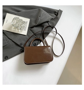 Sac à main chic en cuir verni marron avec bandoulière sur costume gris et livre d'art