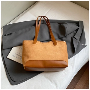 Detail of tan suede tote bag with leather piping on white linen and charcoal blazer