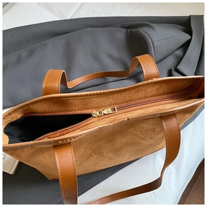 Detailed view of brown suede tote bag with golden zipper and black fabric lining