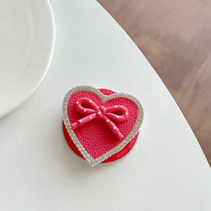 Macro detail of heart-shaped phone grip with leather texture, bow, and rhinestones