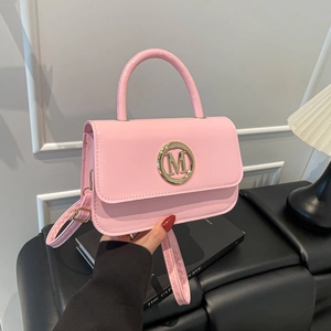 Sac à main en cuir verni rose avec logo M doré sur fond mural blanc