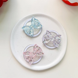Three magnetic glitter bow phone grips in blue, purple, and pink on a ceramic tray