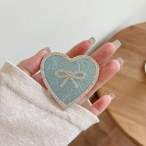 Close-up of heart-shaped phone grip with blue texture, white rhinestones and a bow knot