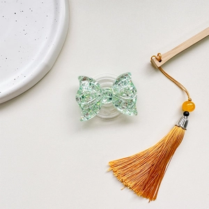 Detail shot of a glittery mint green butterfly phone grip with soft yellow tassels