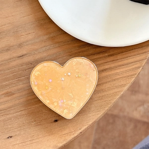 Macro shot of heart-shaped phone grip with glitter and star sequins on a wooden desk