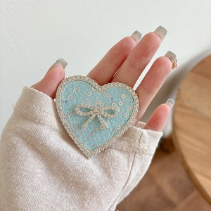 Close-up of heart-shaped phone grip with sequins and rhinestone bow held in hand