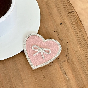 Close-up of heart-shaped pink leather phone socket with sparkling rhinestone bow on wood