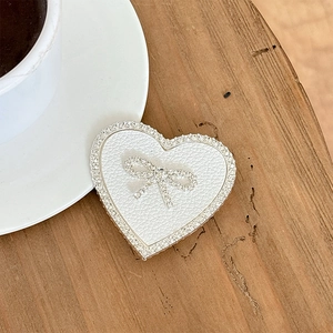 Macro shot of heart-shaped phone grip with leather texture, rhinestones, and bow on a desk